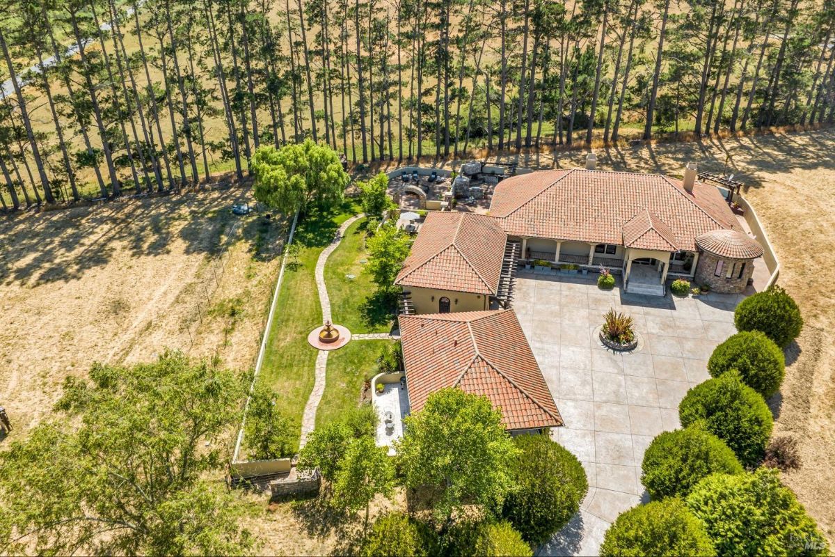 Aerial view of a Spanish-style house with a tiled roof, a landscaped yard, and surrounding trees.