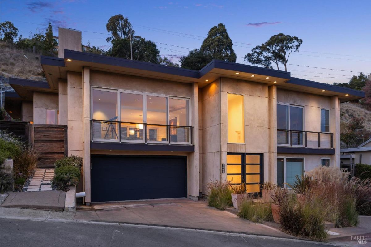 Modern house with large windows and warm lighting during dusk.