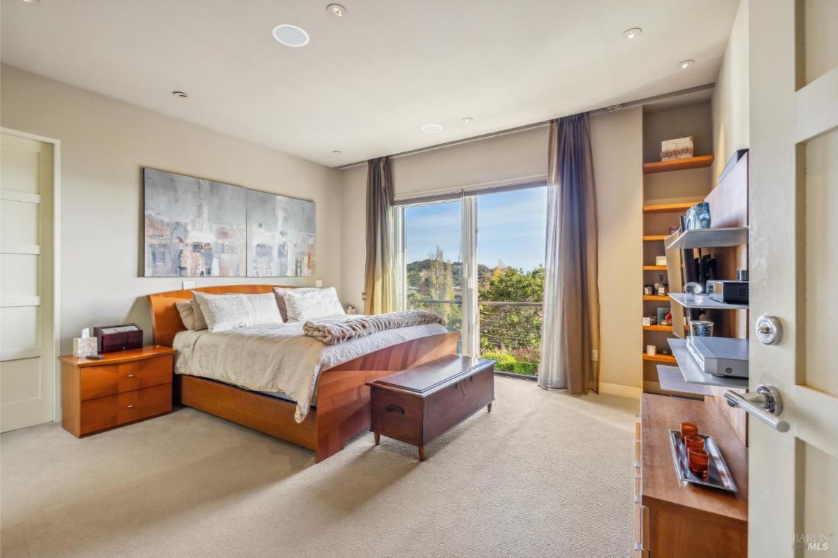 Well-lit bedroom with floor-to-ceiling windows and sliding doors opening to a scenic view.