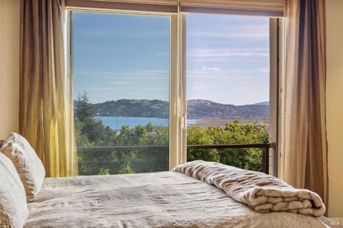 Bedroom with a view of a lake and hills visible through a glass door.