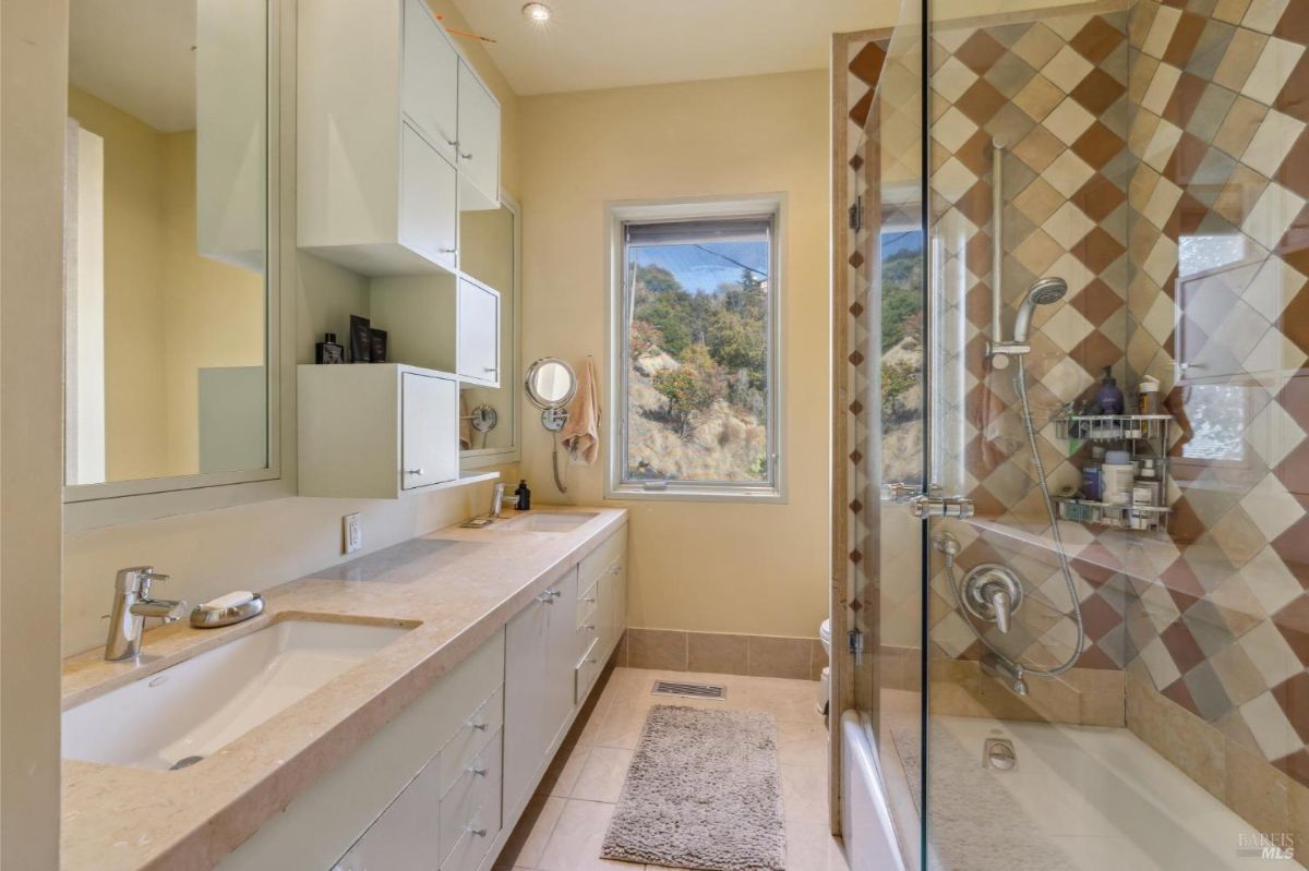 Bathroom with double vanity, storage cabinets, and a glass shower with patterned tiles.