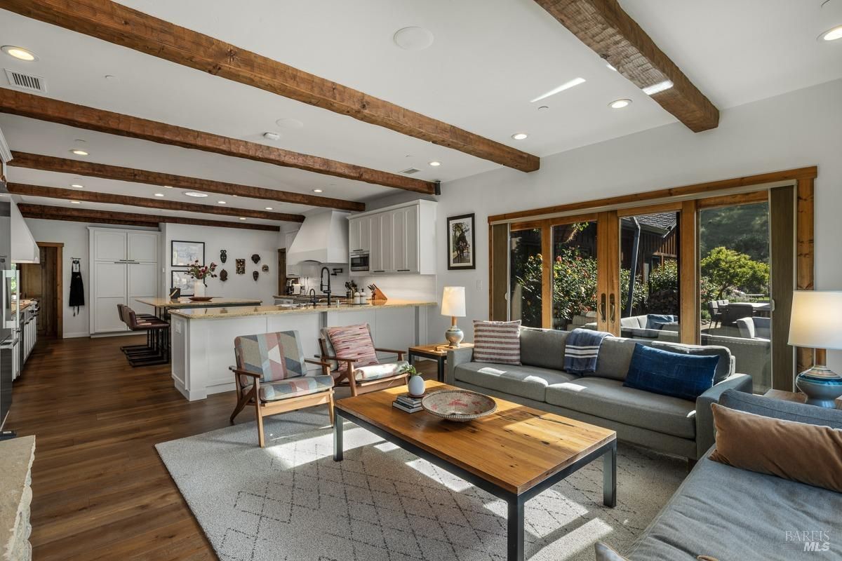 A spacious and open-concept living area with a large kitchen, a cozy living room, and a dining area. The room features exposed wooden beams, large windows, and a fireplace. The overall atmosphere is warm and inviting, perfect for entertaining guests or relaxing with family.