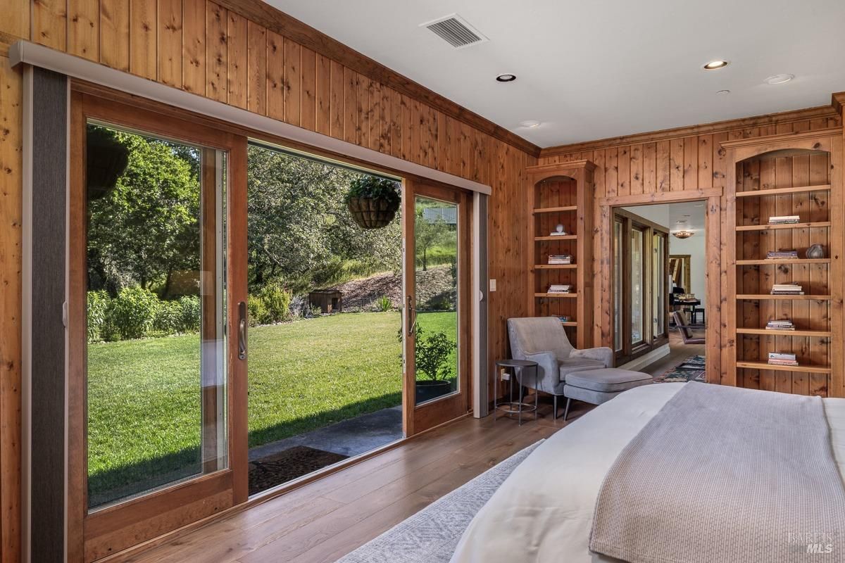  A simple yet inviting bedroom with mustard-yellow accent pillows on the bed, a natural wood headboard, and a door opening to an outdoor seating area.