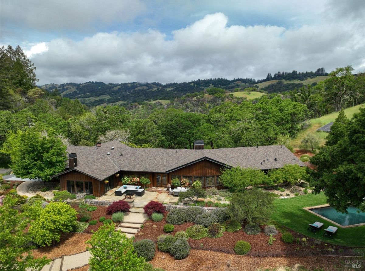 A sprawling, ranch-style home sits nestled amidst rolling hills and lush greenery. The house boasts a large patio and a swimming pool, perfect for enjoying the beautiful surroundings.