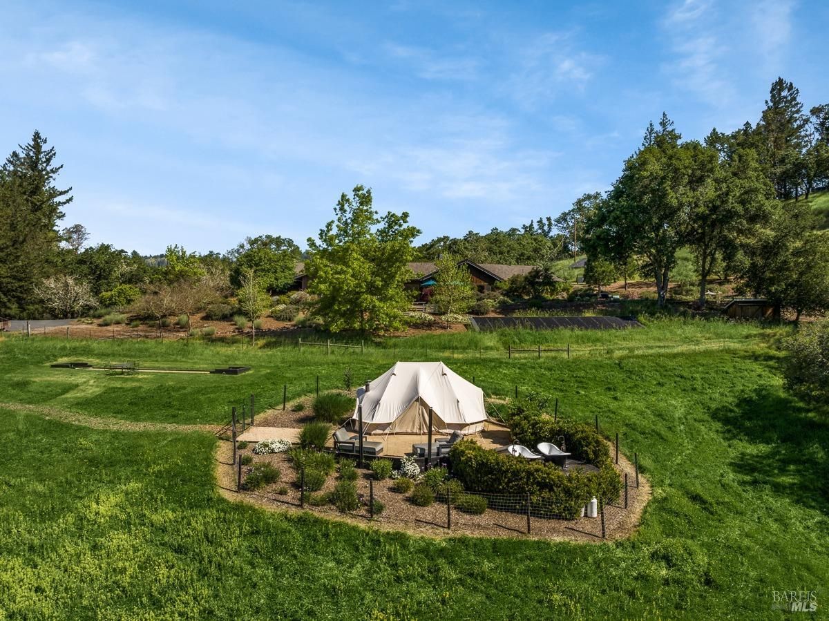 A luxurious glamping tent sits nestled amidst a lush green field, surrounded by towering trees and a picturesque landscape.