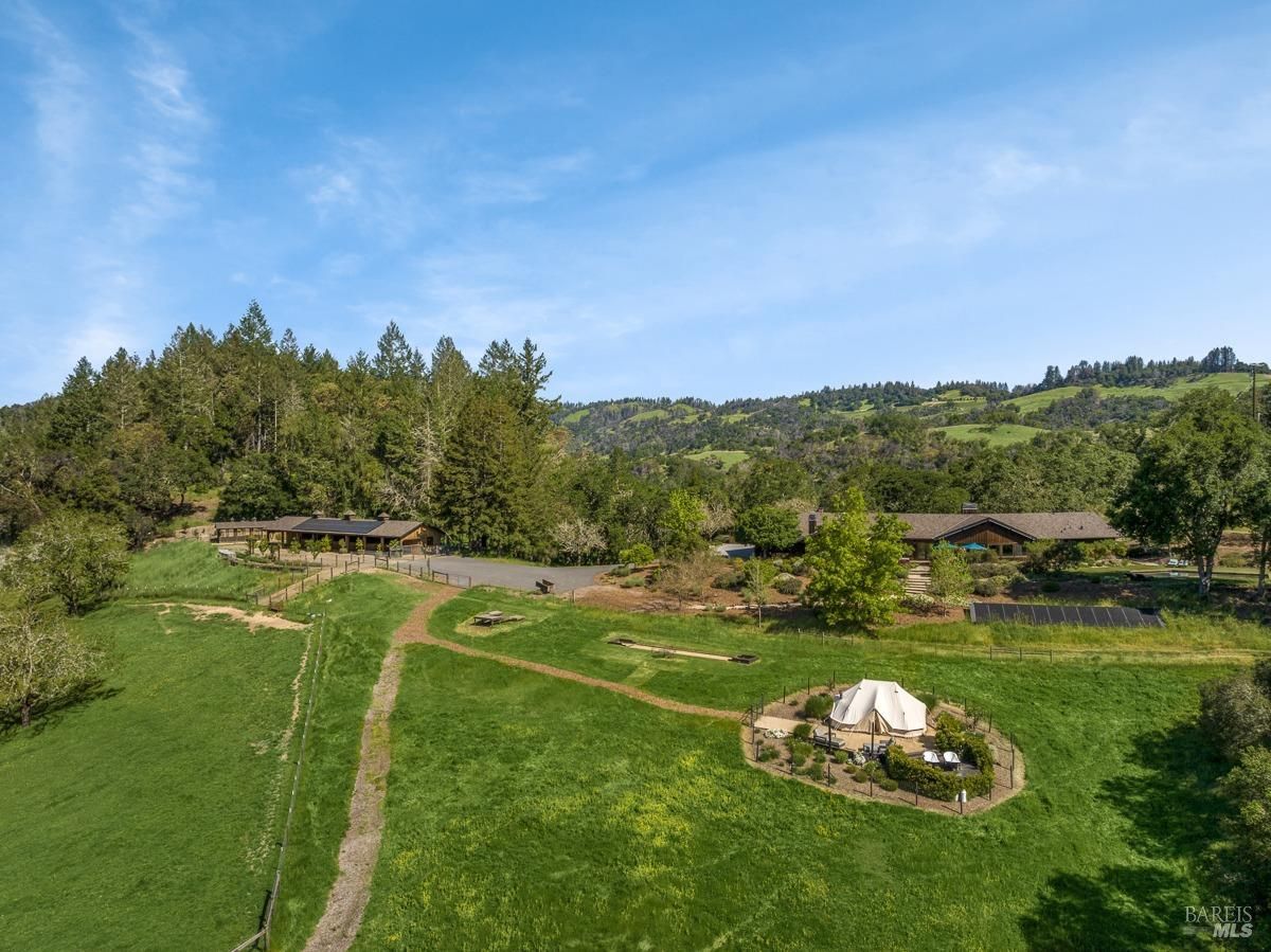 A luxurious glamping tent sits nestled amidst a lush green field, surrounded by towering trees and a picturesque landscape.