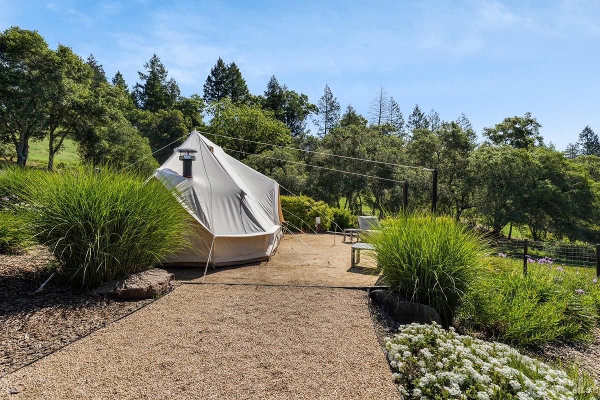 A luxurious glamping tent sits nestled amidst a lush green field, surrounded by towering trees and a picturesque landscape.