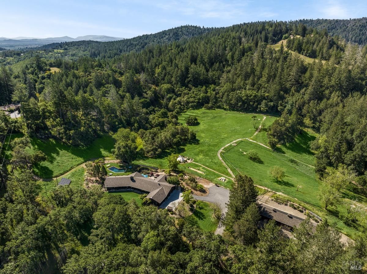 A sprawling ranch house nestled amidst rolling hills and lush greenery. The property boasts a large lawn, a swimming pool, and a scenic view of the surrounding landscape.