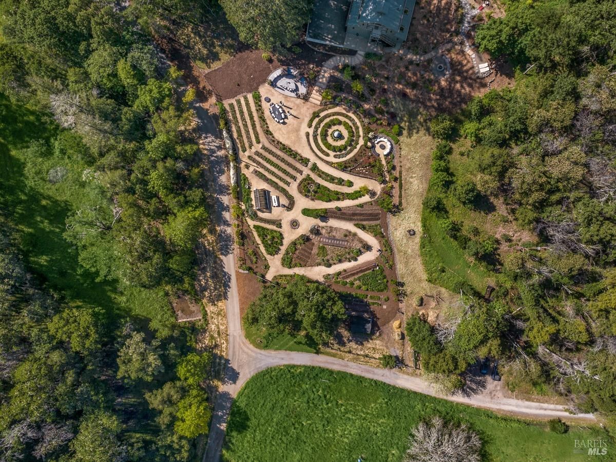 An aerial view of a beautifully landscaped garden with intricate patterns and various plant life. The garden appears to be a work of art, with winding paths and circular beds creating a harmonious design.