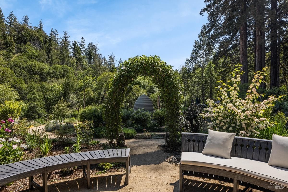 A picturesque garden path leads through a lush, green landscape. A charming arched trellis covered in vines frames the view, inviting you to explore further.