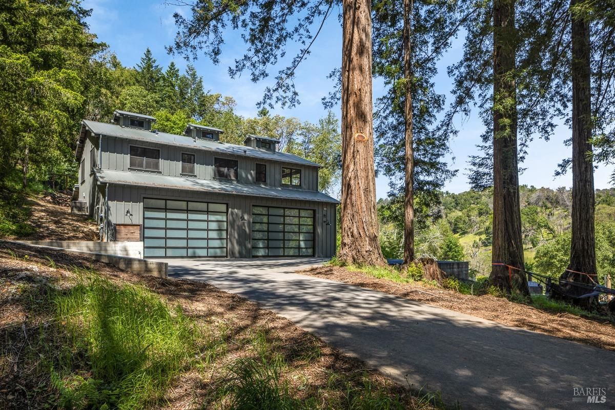 A modern barn-like structure with large glass doors and a metal roof. The building is surrounded by tall trees, creating a rustic yet contemporary architectural feel.