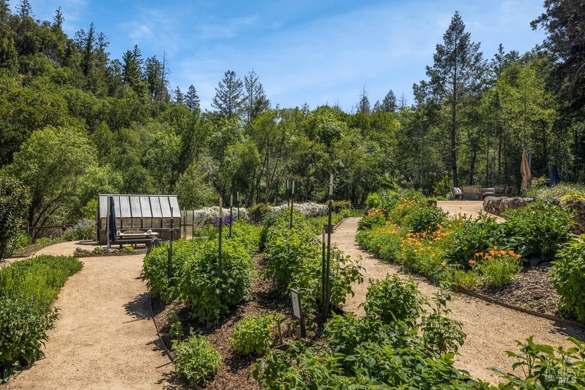 A beautiful garden with winding paths, lush greenery, and a variety of colorful flowers. A small greenhouse adds a touch of charm to the scene.