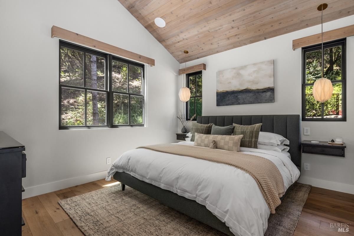  Another cozy bedroom with large windows framing outdoor greenery. The vaulted ceiling and minimalist furniture create a serene retreat-like feel.