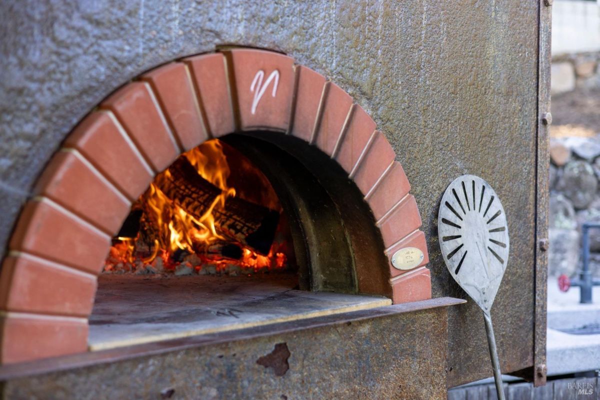 A close-up of a rustic wood-fired oven, showcasing its brick arch and roaring fire. The oven is ideal for outdoor cooking, adding a traditional charm to the setup.