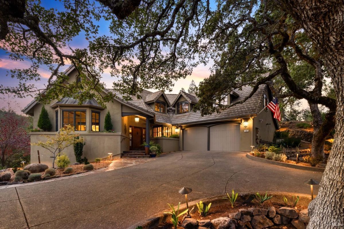 Large two-story house with multiple gables, a curved driveway, and surrounded by mature trees.