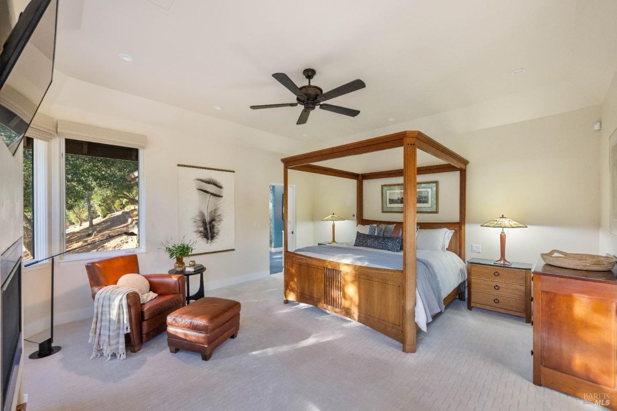 Master bedroom featuring a four-poster bed, seating area, and large windows overlooking trees.