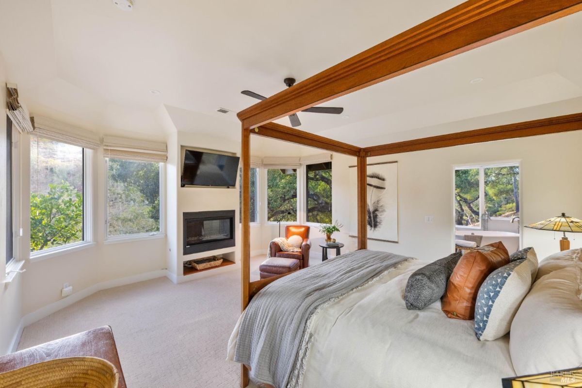 Bedroom with a four-poster bed, a fireplace, and large windows with natural light.