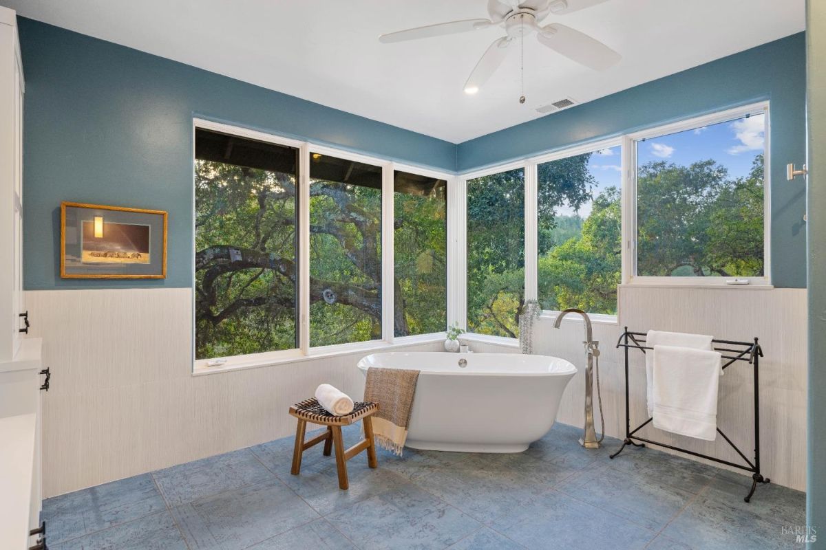 Bathroom with a freestanding bathtub, blue walls, and large windows showcasing outdoor views.