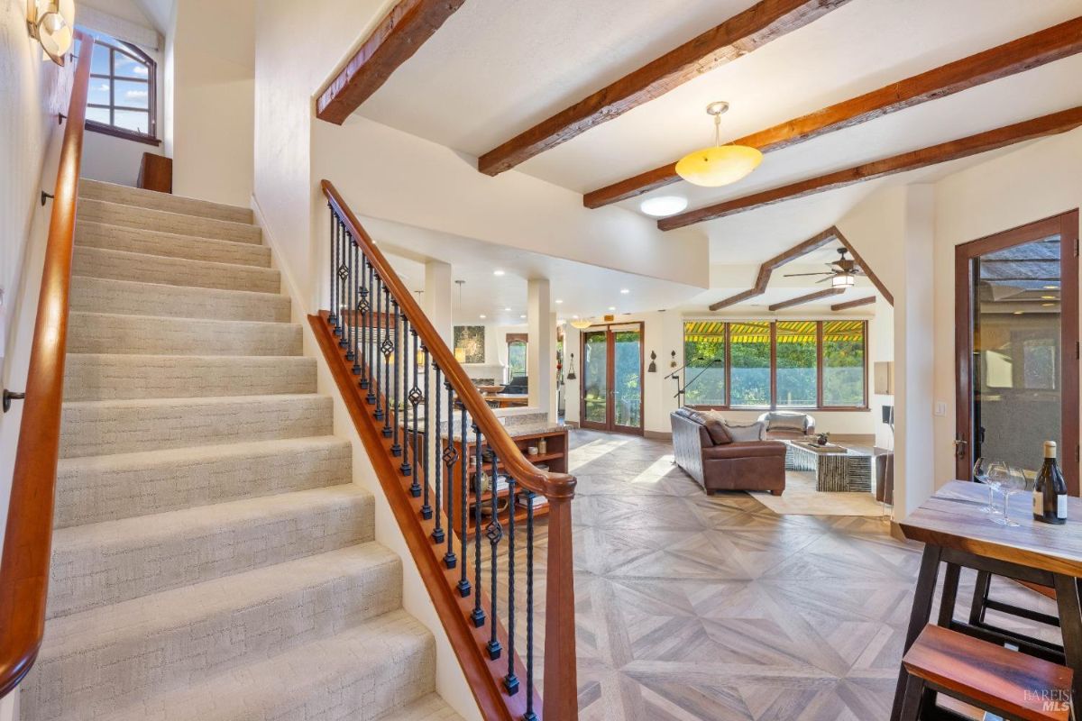 Staircase with wooden railings and wrought iron balusters, leading to an open floor plan with exposed beams.