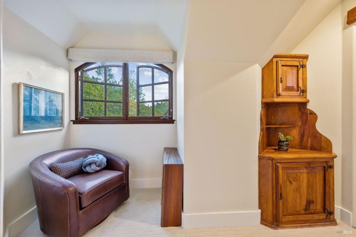 Cozy reading nook with a leather chair, a wooden cabinet, and a window view of greenery.