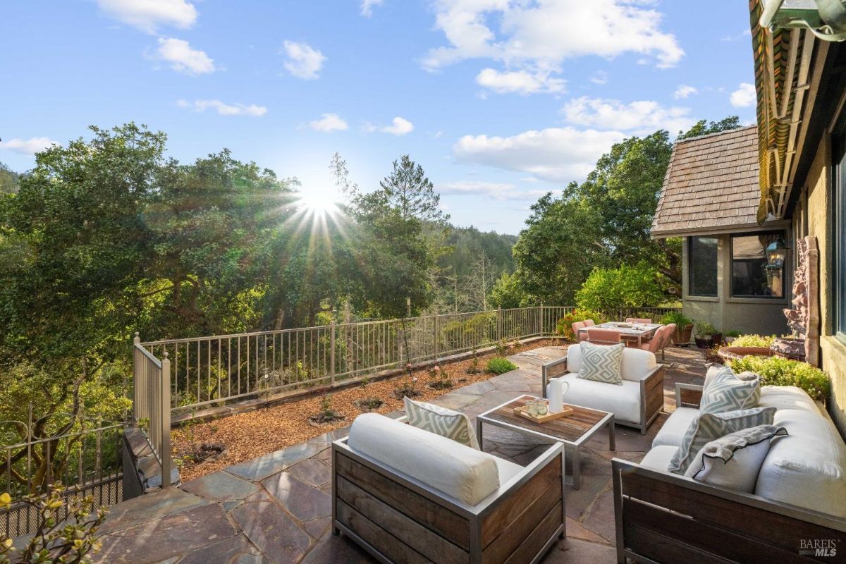 Outdoor patio with cushioned seating, a stone floor, and a view of surrounding trees.