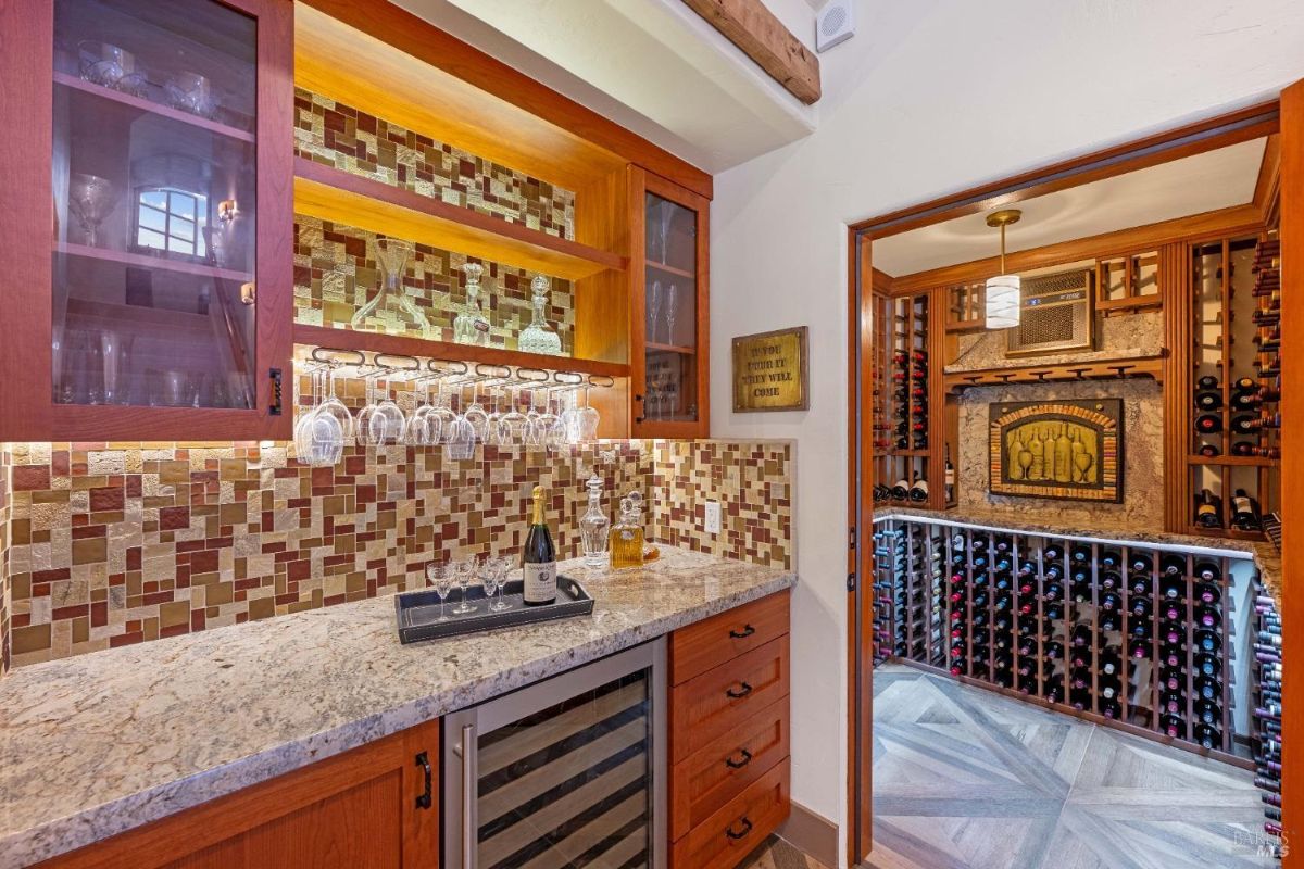 Wet bar area with a mosaic backsplash, glassware storage, and a connected wine cellar.