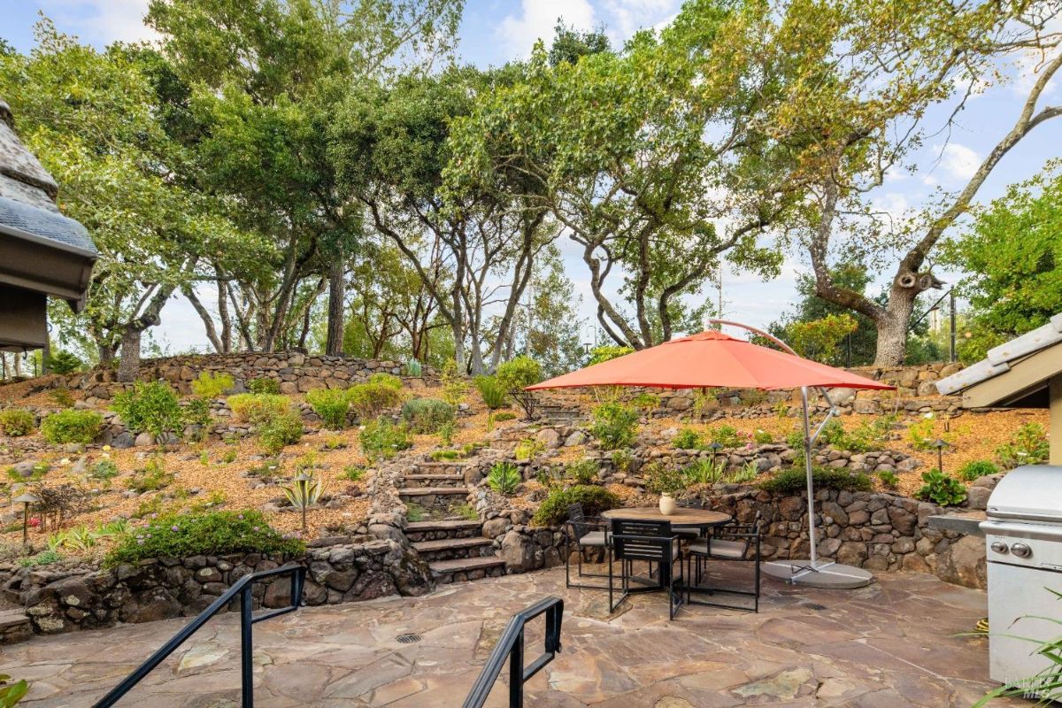 Backyard with a stone patio, outdoor dining set under an umbrella, and terraced landscaping.