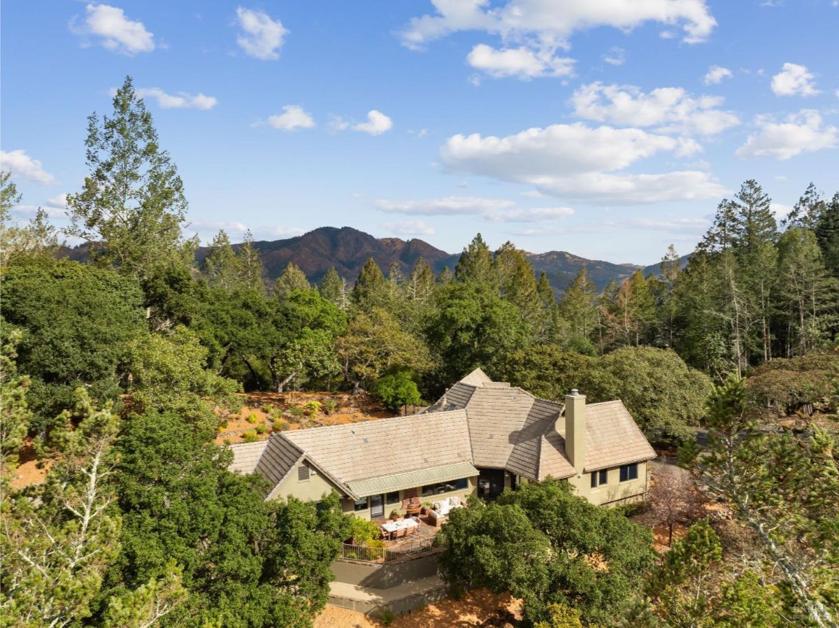 Aerial view of a house surrounded by forested hills and mountains in the distance.