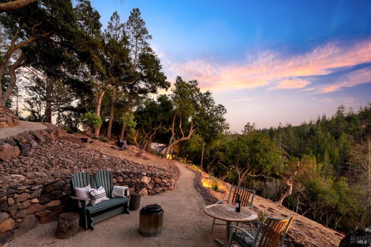 Rustic outdoor seating area along a gravel path with a backdrop of trees at sunset.