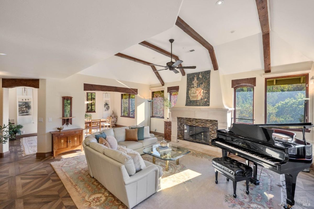 Spacious living room with a vaulted ceiling, exposed wooden beams, a fireplace, and a grand piano.