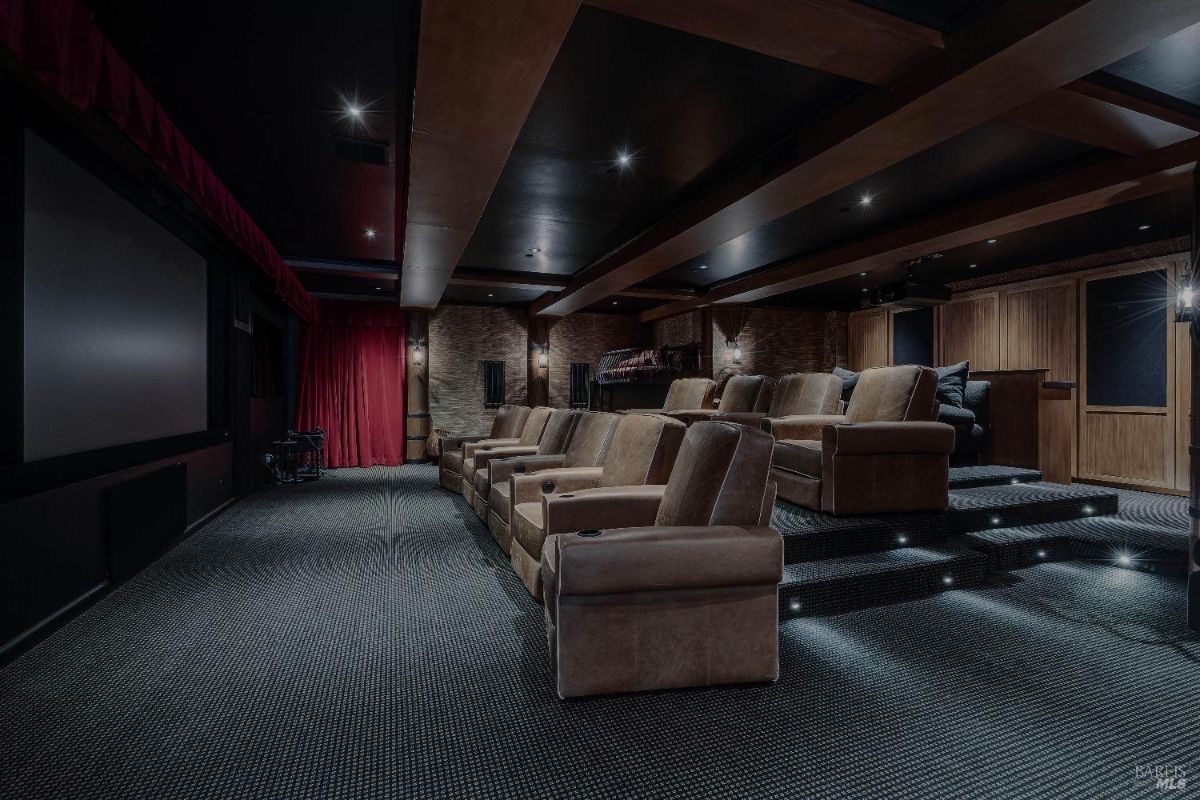 Home theater room is designed for a truly immersive cinematic experience. Plush tiered seating, complete with individual reclining chairs, ensures comfort for all viewers. The dark walls and ceiling, along with the dramatic lighting, create an ambiance that rivals a commercial cinema. This is a space for movie lovers to indulge in their passion in the comfort of their own home.