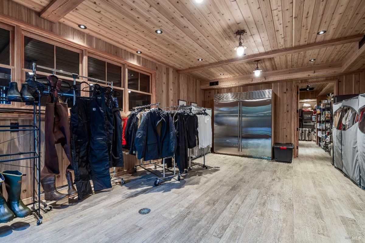 This well-organized mudroom and storage area is designed for practicality and functionality. With ample space for hanging outdoor gear, storing boots and equipment, and even a large refrigerator, it's ideal for keeping a busy household organized and prepared for any adventure. The wood paneling and flooring add a touch of rustic warmth to the space.