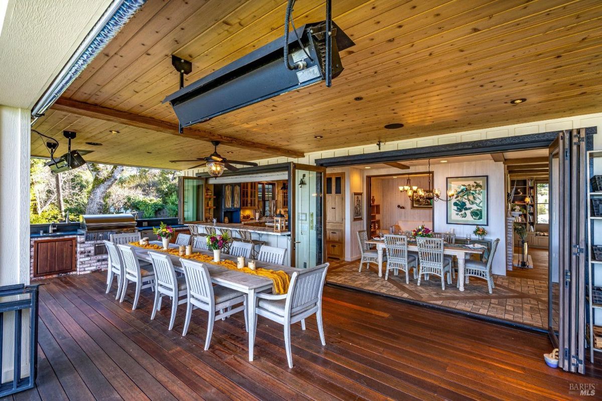 The open concept design seamlessly connects the interior dining area with the expansive deck, creating a large and airy space perfect for hosting gatherings. The deck is equipped with a long dining table, ample seating, and a full outdoor kitchen and bar, ensuring that guests can comfortably enjoy meals and socialize while taking in the surrounding views.