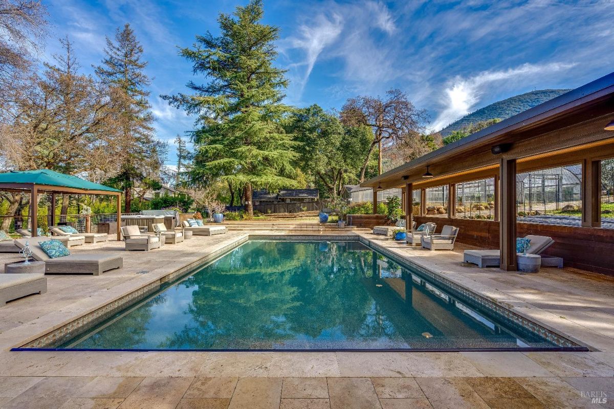 The sparkling pool is surrounded by ample seating and a covered patio, providing comfortable spaces to lounge and socialize. The surrounding trees and lush greenery create a sense of privacy and tranquility, while the mountain backdrop adds to the scenic beauty. With a separate gazebo and a hot tub tucked away in the corner, this backyard offers a variety of options for enjoying the outdoors.