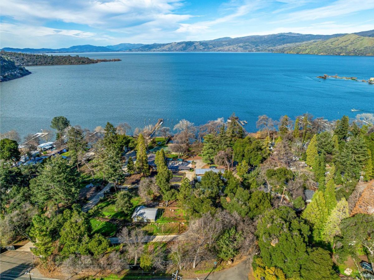 This aerial shot captures a peaceful lakeside community nestled amidst a lush landscape. Homes are dotted amongst the greenery, enjoying proximity to the serene waterfront. A private dock extends into the calm waters, offering residents a place to moor their boats and soak in the tranquil beauty of their surroundings. The overall scene evokes a sense of serenity and escape, a perfect blend of nature and comfortable living.