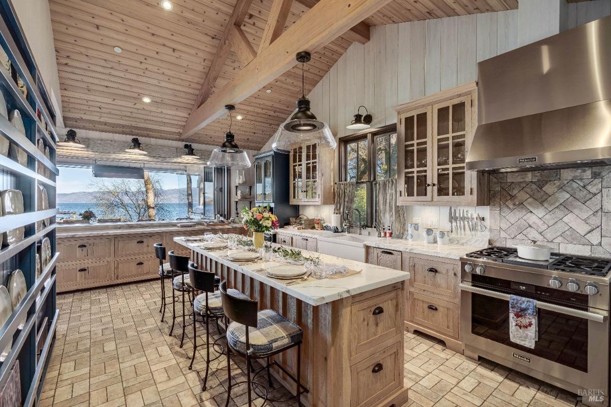 This expansive kitchen is a chef's dream, boasting ample counter space, custom cabinetry, and high-end appliances. The large island provides a perfect space for meal preparation and casual dining, while the exposed beams and warm wood tones create a rustic yet elegant atmosphere. Large windows offer stunning views, bringing the beauty of the outdoors into the heart of the home.