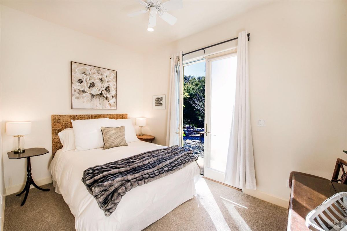 Bright and airy bedroom with a queen-sized bed, a large painting on the wall, and a pair of sliding glass doors leading to a patio.