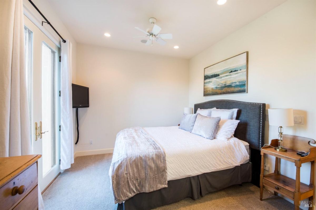 Bedroom with a king-sized bed, a large painting on the wall, and a pair of doors leading to a balcony.