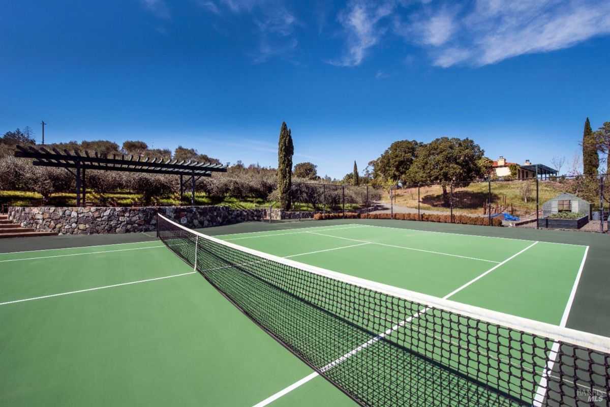 Rectangular green tennis court with net in the middle surrounded by trees