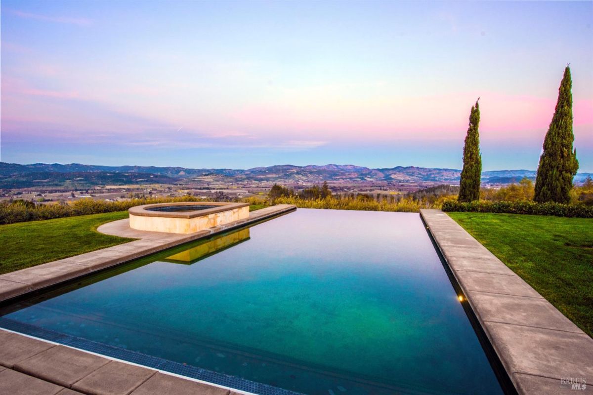 Large infinity pool with a hot tub overlooking a scenic valley at sunset.