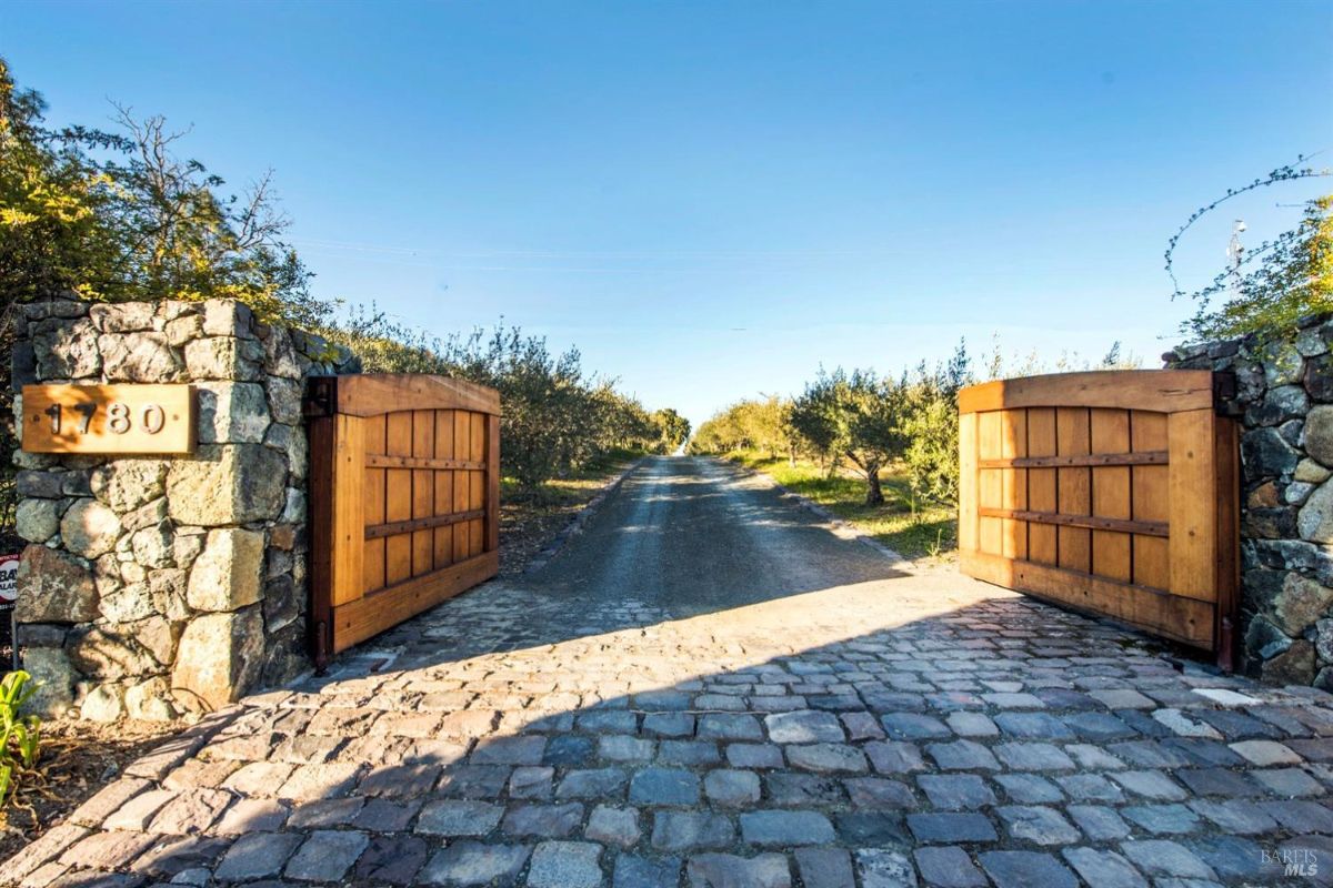 Close-up view features the house’s gated driveway with cobblestone paving and wooden gates.