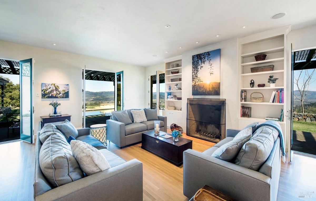 Living room showcases modern furniture, built-in shelves, and a fireplace with large windows.