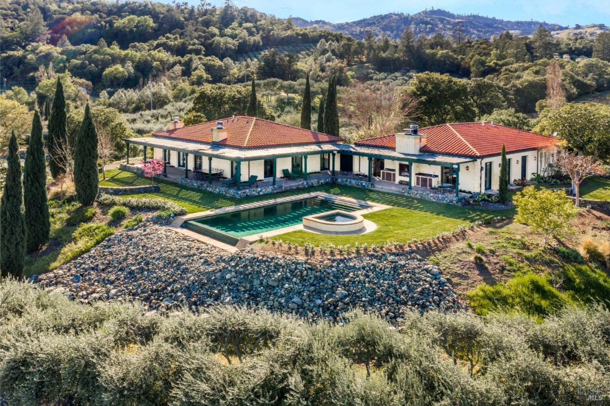 A luxurious house surrounded by hills with a rectangular pool in the backyard.