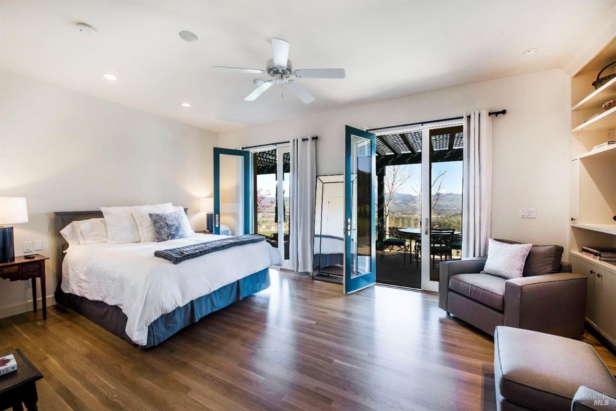 Bedroom with a king-sized bed, a pair of doors leading to a balcony, and a seating area with a chair and a bookshelf.