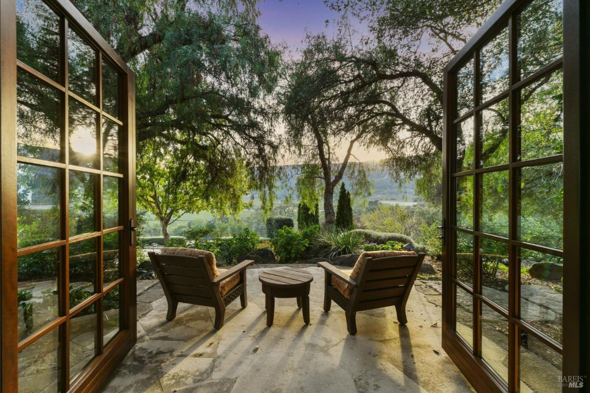 A patio with two lounge chairs and a circular table, surrounded by trees and overlooking a scenic valley.