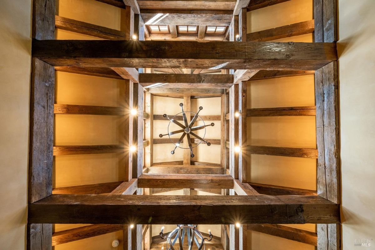 Ceiling view showcasing exposed wooden beams and a central chandelier in a geometric arrangement, creating a warm architectural feature with integrated lighting.