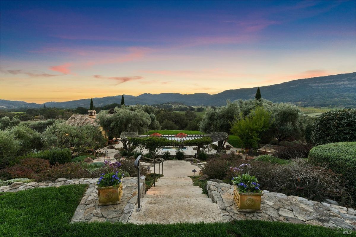 Landscaped garden with a pathway and stone steps leading to a pergola overlooking a valley.