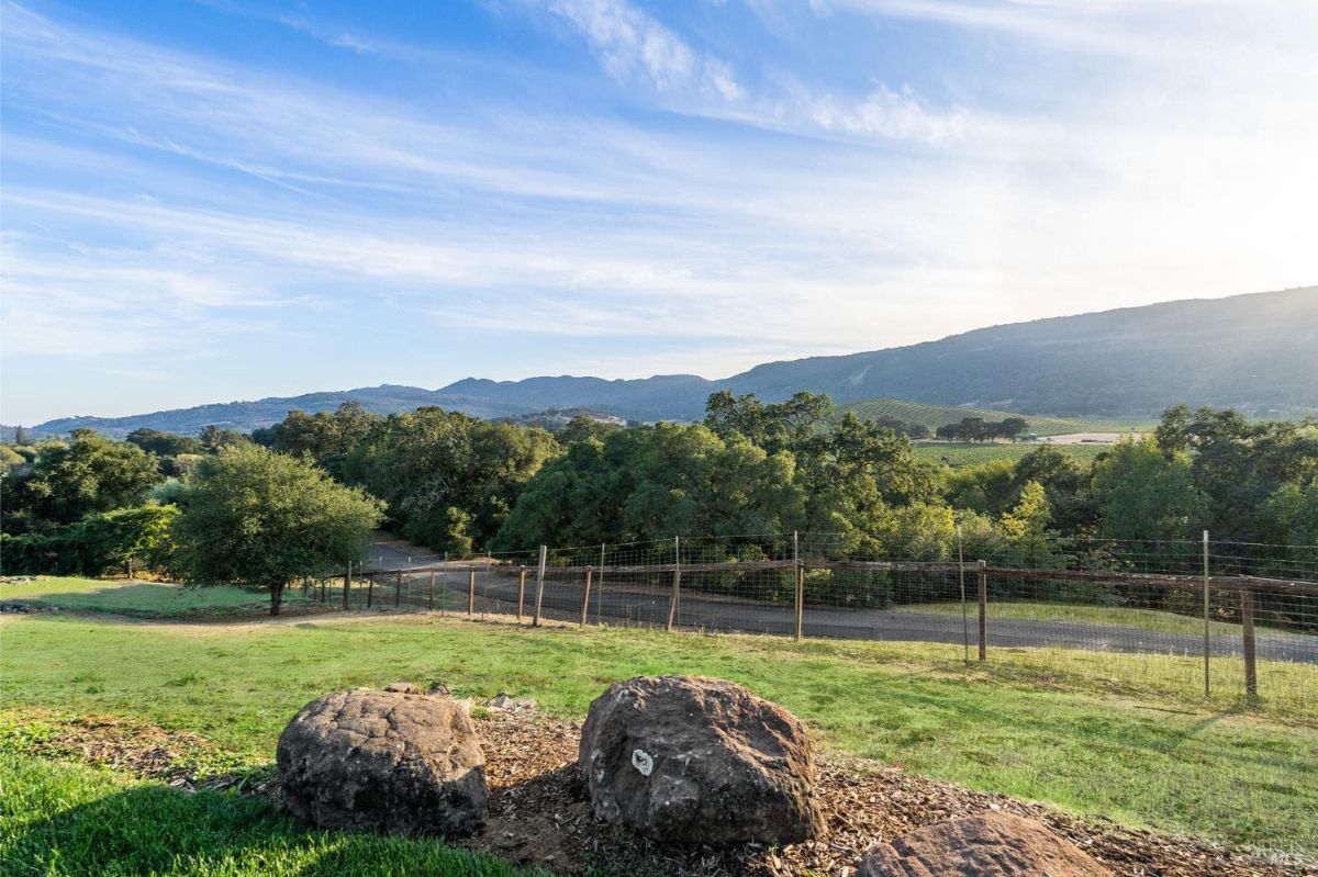 Open grassy field bordered by fencing and a wooden gate. Hills and trees form the backdrop. 