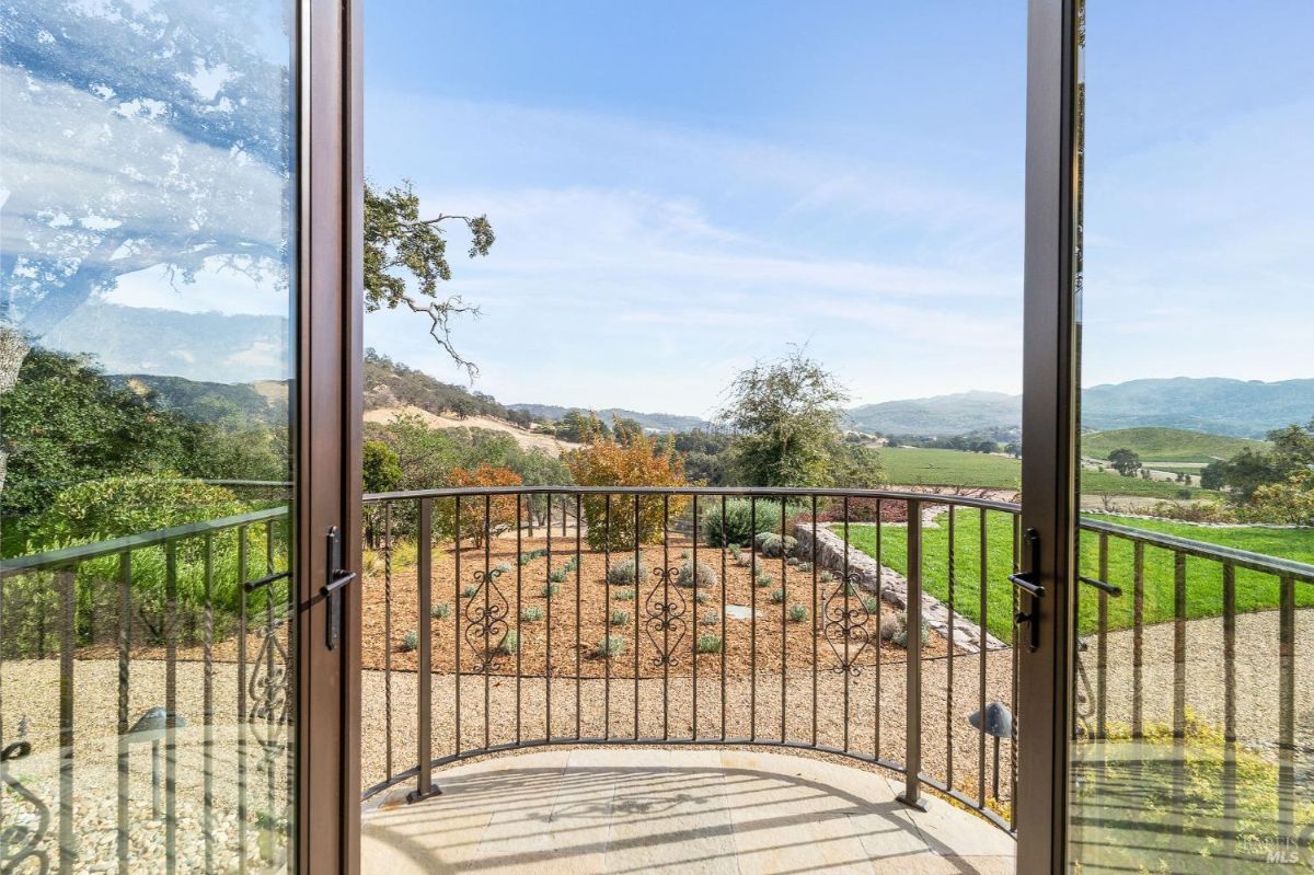  A balcony with a wrought iron railing, overlooking a landscaped area and distant rolling hills.