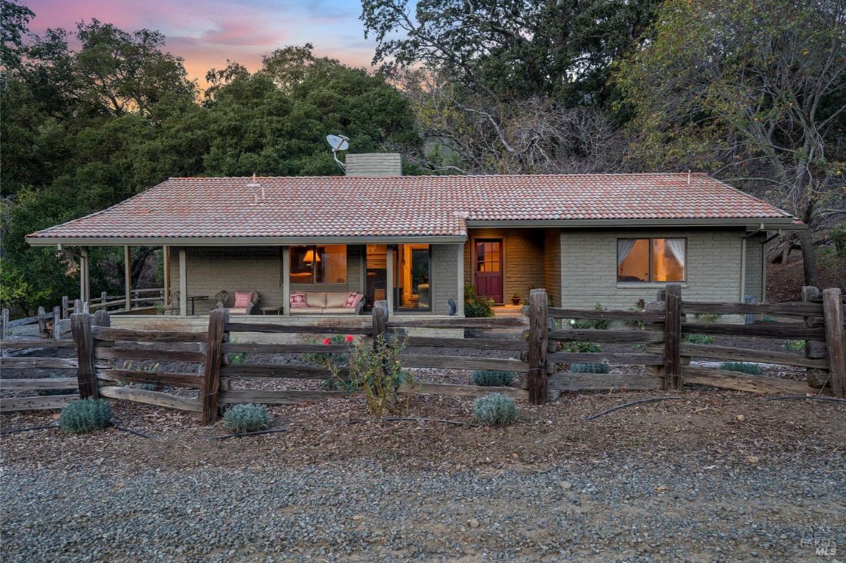 A single-story ranch-style house with a tile roof, a wooden fence, and surrounded by trees.